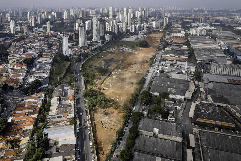 Imagem aérea mostra um grande terreno cercado por prédios, à esquerda, e por galpões, à direita