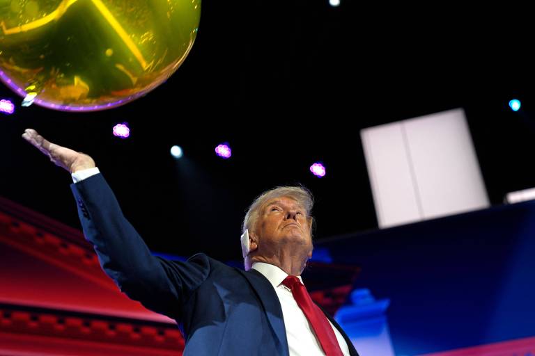 A imagem mostra um homem de terno azul e gravata vermelha empurrando um balão dourado. O fundo é escuro com luzes coloridas e formas geométricas iluminadas.
