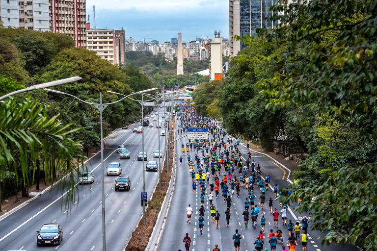 Maratona de inverno SP City, 2022. Várias pessoas correm no meio de uma avenida em São Paulo.