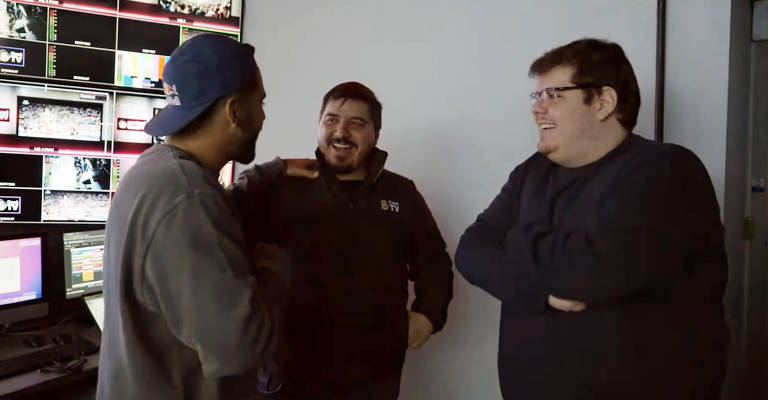 Pedro Scooby e Luis Felipe Freitas conversam com Casimiro Miguel em uma sala cheia de televisores na Cazé TV