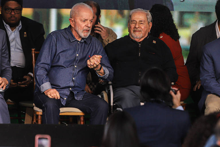 Lula segura a mão de Raduan sentado ao seu lado em um palco