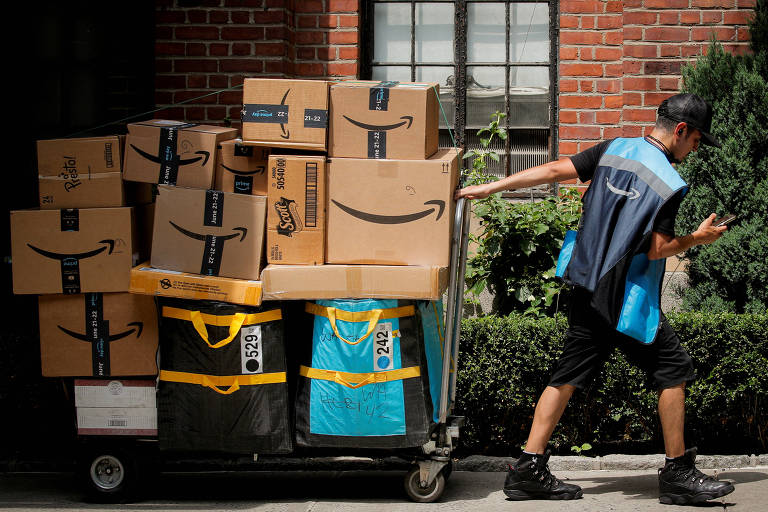 Um entregador da Amazon puxa carrinho de entrega cheio de pacotes com o logotipo da Amazon