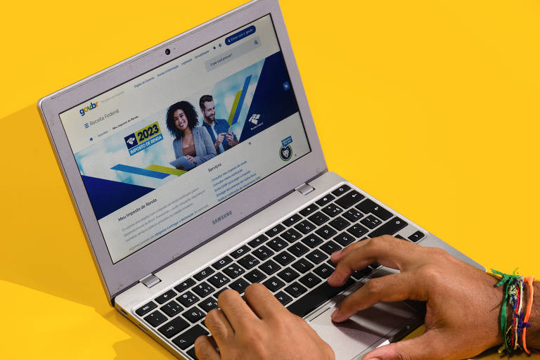 A imagem mostra um laptop aberto com uma tela exibindo um site. O fundo é amarelo. As mãos de uma pessoa estão digitando no teclado. Na tela, há imagens de duas pessoas e elementos gráficos coloridos.