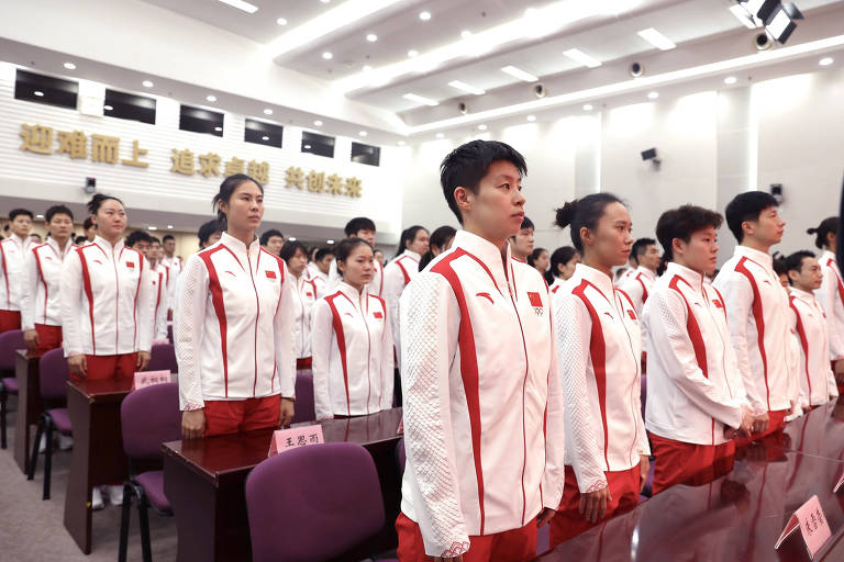 Foto mostra uma visão geral da reunião inaugural da delegação chinesa para os Jogos Olímpicos de Paris 2024 em Pequim, capital da China. Dezenas de atletas chineses estão com agasalhos brancos, com detalhes vermelhos, e calças também vermelhas. 