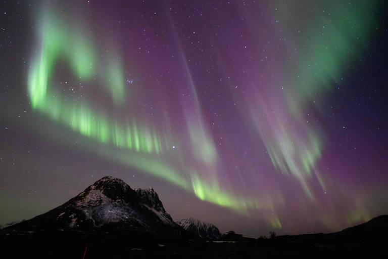 Aurora boreal verde e roxa sob um pico de uma montanha