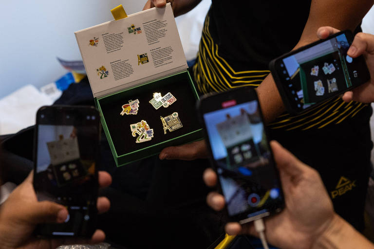 Atletas brasileiros fotografam broches comemorativos entregues à delegação
