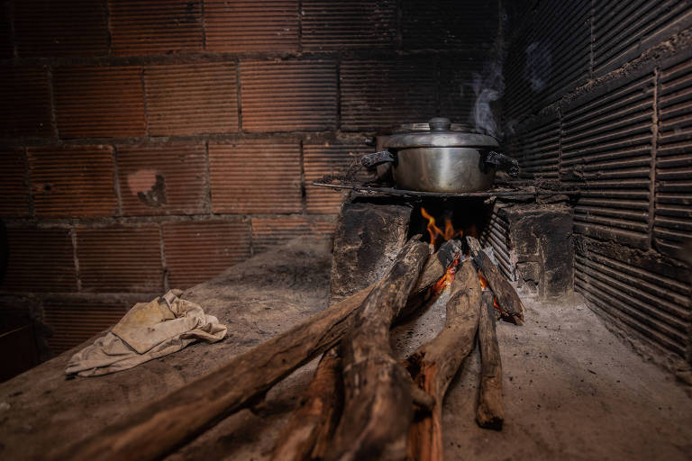 Lenha queimando em fogão improvisado, onde se vê uma panela velha 