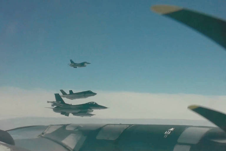 Três aviões menores são vistos do lado do motor de um avião maior. O céu está azul e há faixas de nuvens brancas 