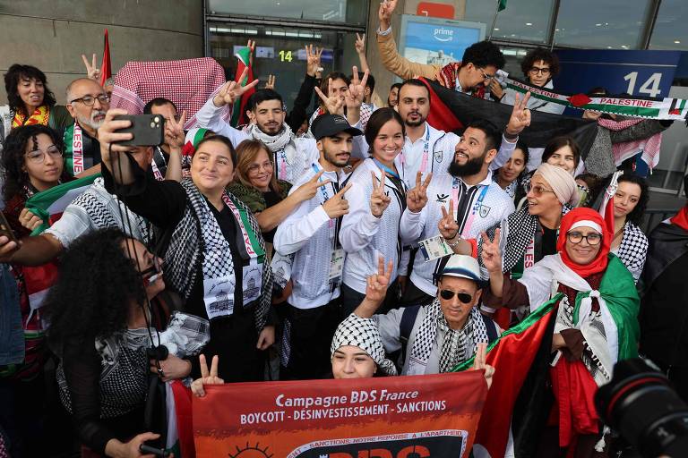 Ativistas se reunem vestindo roupas tradicionais e segurando faixas e a bandeira palestina