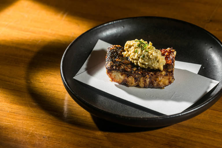 Em uma mesa de madeira, um prato de cor escura abriga um tempura de enguia com maionese
de ovos