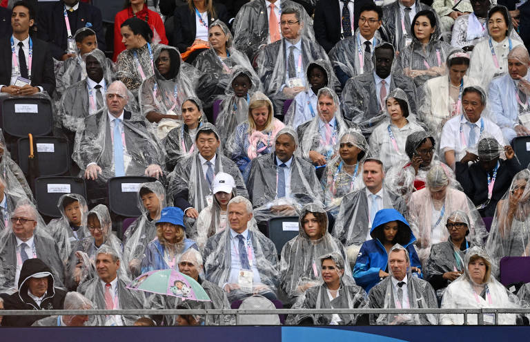 Espectadores da cerimônia usam capas de chuva para se proteger durante a cerimônia
