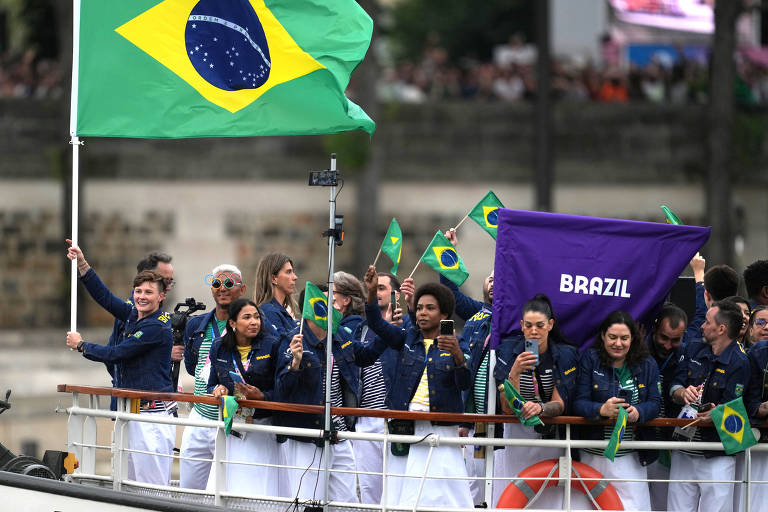 Raquel Kochhann, do rúgbi, uma das porta-bandeiras na cerimônia de abertura de Paris 2024, vai à frente da delegação do Brasil, segurando bandeira do país, no barco Bel Ami, no rio Sena