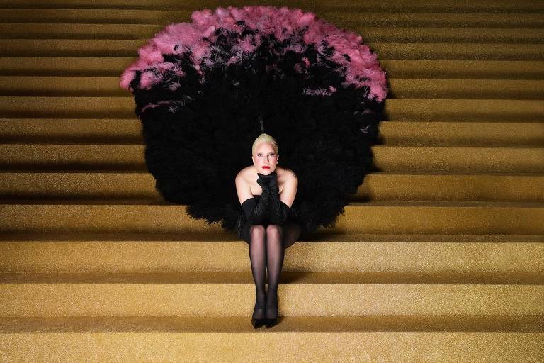 A cantora americana Lady Gaga usa uma fantasia com plumas e está sentada em escadaria