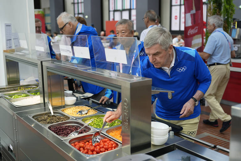 O presidente do Comitê Olímpico Internacional (COI), Thomas Bach (em primeiro plano), serve-se de tomatinhos em refeitório da Vila Olímpica de Paris