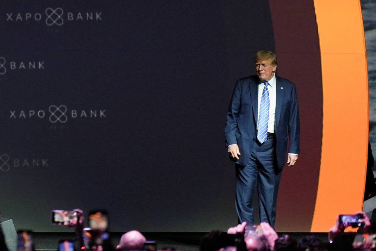 Na foto, Trump está de terno escuro, camisa branca e gravata azul claro em um palco