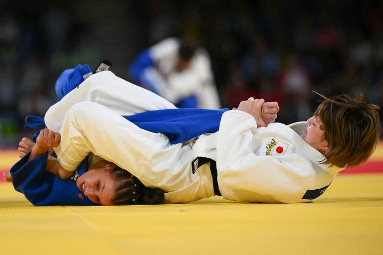 A judoca Natasha Ferreira, usando quimono azul, leva golpe da japonesa Natsumi Tsunoda, que veste branco, na categoria até 48 kg nas Olimpíadas de Paris
