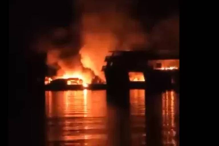 a imagem é a reprodução de um vídeo e mostra a carcaça de um barco pegando fogo sob as águas do Rio Negro, está escuro e só é possível identificar as chamas