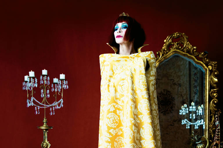 mulher ruiva de cara pintada de branco e azul com candelabros e espelhos nobres a seu redor