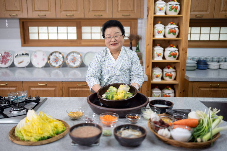Em uma cozinha, mulher coreana mostra verduras