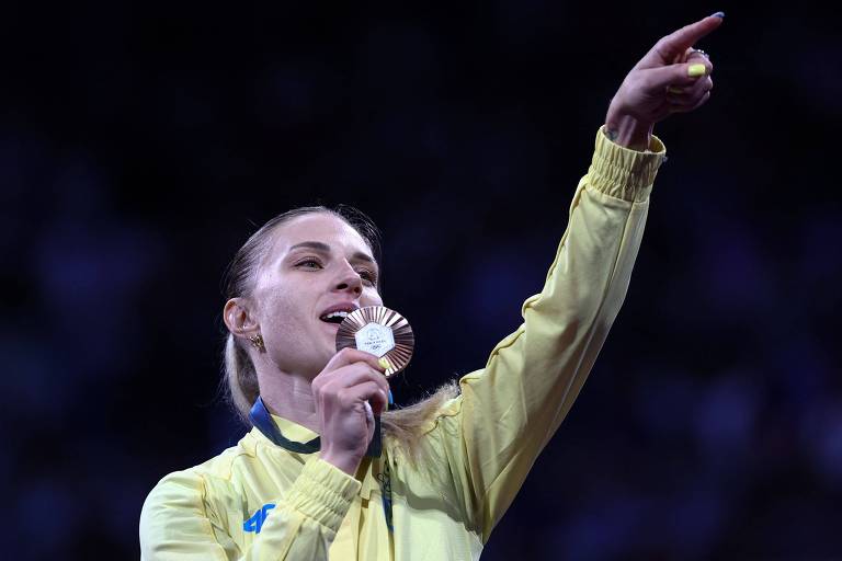 A esgrimista ucraniana Olga Kharlan aponta para o público com o dedo indicador da mão esquerda ao receber a medalha de bronze, que segura com a mão direita, na prova individual de sabre das Olimpíadas de Paris