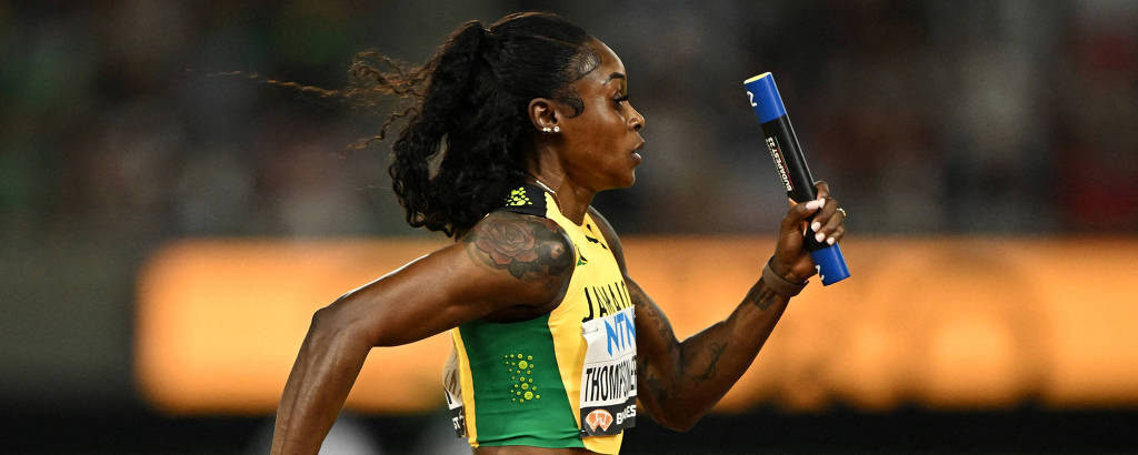 Atleta Elaine Thompson-Herah está correndo em uma pista, segurando um bastão de revezamento azul. Ela usa um uniforme amarelo e verde, representando a Jamaica.