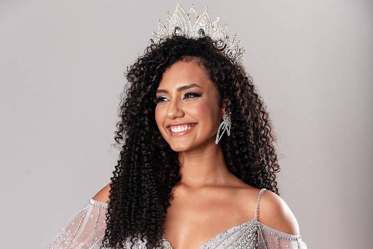 Maria Vitória Rondon posa para foto com coroa na cabeça. Ela está usando um vestido prateado e está sorrindo. 