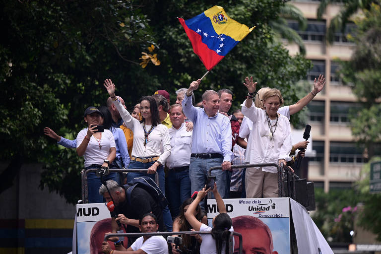 A líder opositora María Corina Machado (de blusa branca e colar) e Edmundo González (de camisa azul e bandeira na mão) durante ato em Caracas