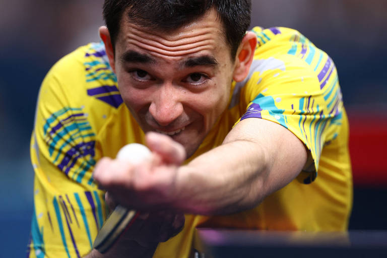 O mesa-tenista brasileiro Hugo Calderano olha a bolinha ao se preparar para sacar contra o espanhol Alvaro Robles nas Olimpíadas de Paris