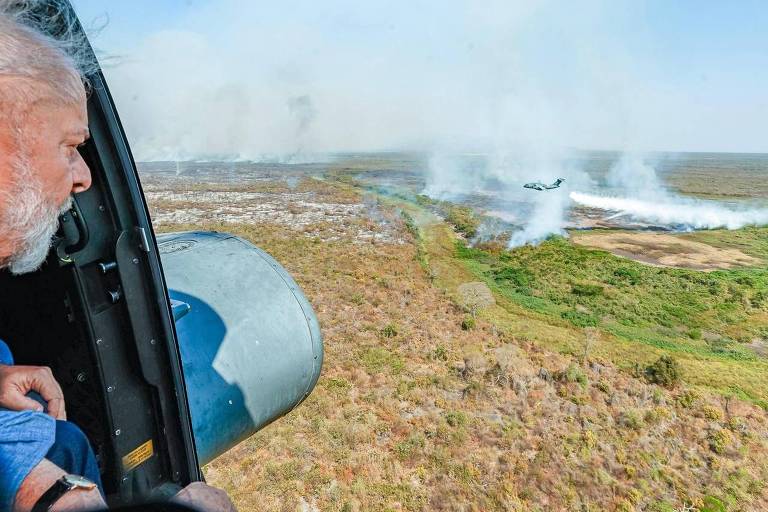 Lula observa fumaça subindo de planície por meio de aeronave com porta aberta