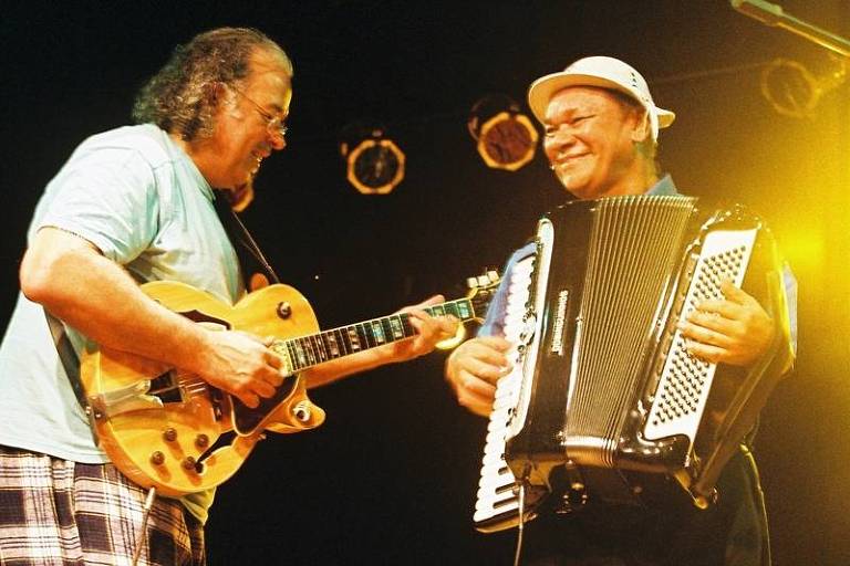 Em foto colorida, Arismar toca guitarra e Dominguinhos sanfona sorrindo