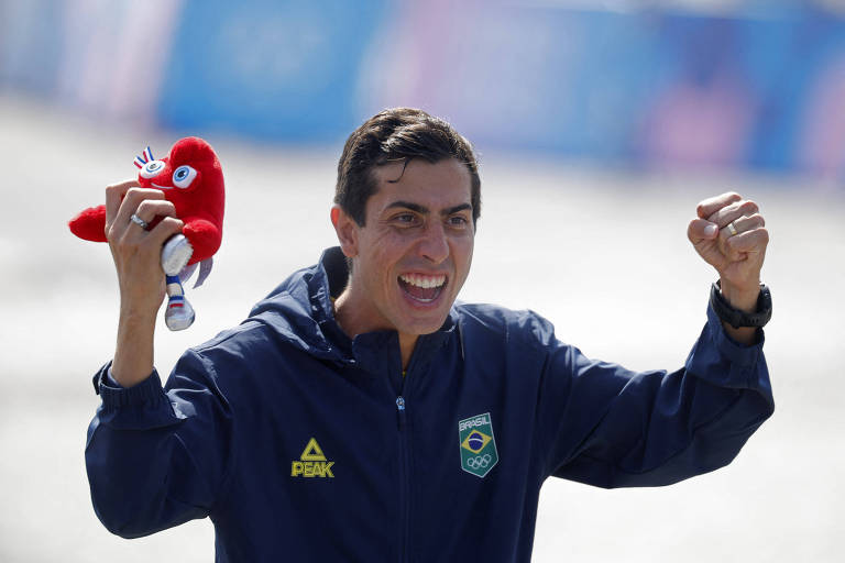 Vibrando, sorrindo e com a mascote olímpica na mão direita, o marchista Caio Bonfim comemora a conquista da medalha de prata na prova dos 20 km nas Olimpíadas de Paris