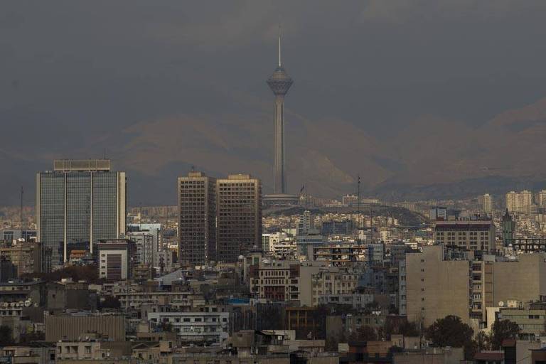 A imagem mostra uma vista panorâmica de Teerã, capital do Irã, com vários edifícios. No centro, destaca-setorre Milad, a sexta mais alta do mundo para telecomunicações 