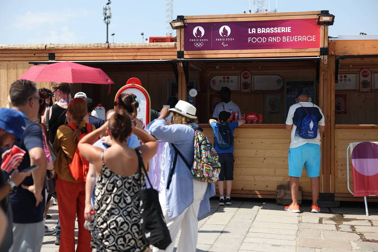 A imagem mostra um quiosque de praia com uma fila de pessoas esperando para ser atendidas. O quiosque é de madeira e possui uma placa na parte superior com o texto 'LE BRASSAGE POUR AMBIANCEURS'. Algumas pessoas estão usando chapéus e roupas de verão, enquanto outras seguram guarda-sóis. O ambiente é ensolarado e há uma atmosfera de lazer.
