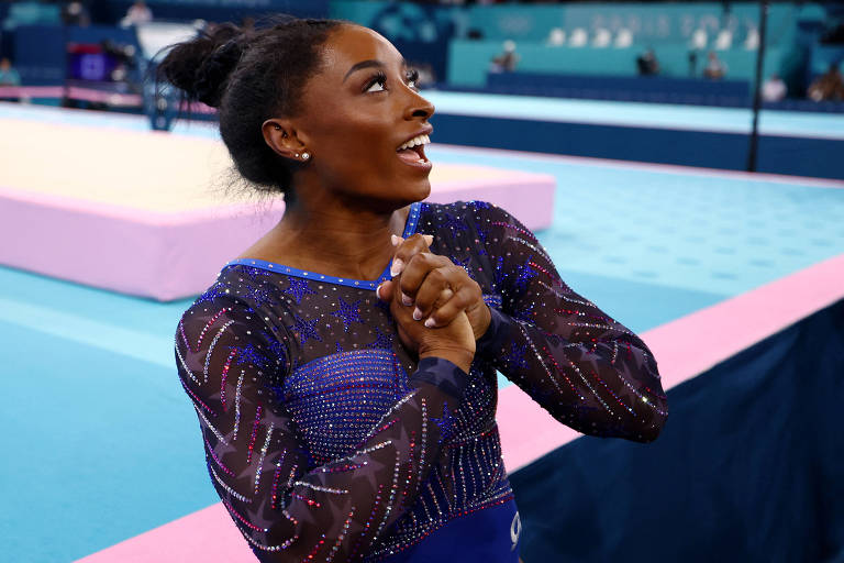 A norte-americana Simone Biles olha para o alto e sorri, com as mãos unidas, na Arena Bercy, local da ginástica artística nas Olimpíadas de Paris
