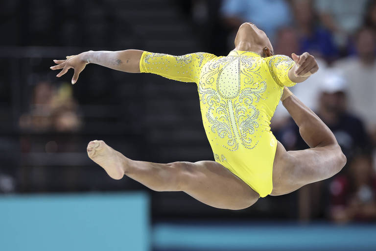 Usando collant amarelo, a ginasta Rebeca Andrade faz movimento com as pernas e as mãos simultaneamente estendidas na final do individual geral nos Jogos Olímpicos de Paris