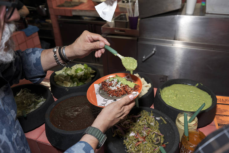 Pessoa coloca molho de pimenta em um taco