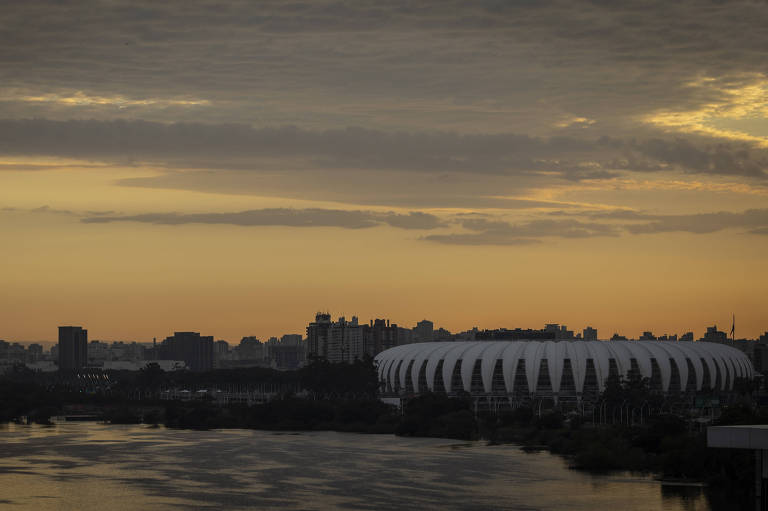 Imagem mostra o horizonte da cidade ao fundo do lado; é possível ver uma grande estrutura de cor branca à direita