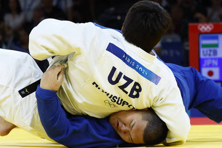 De quimono branco, Alisher Yusopov, do Uzbequistão, pressiona contra o tatame Tatsuru Saito, do Japão, que usa quimono azul, em luta entre pesos-pesados do judô nas Olimpíadas de Paris