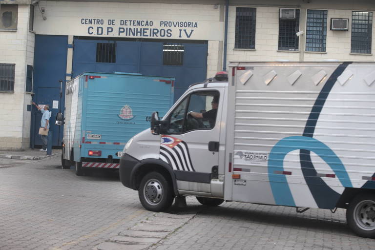 A imagem mostra a entrada do Centro de Detenção Provisória Pinheiros IV, com dois caminhões estacionados. Os veículos são pintados nas cores cinza e azul