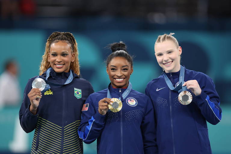 Da esquerda para a direita, no pódio da prova de salto das Olimpíadas de Paris, Rebeca Andrade (prata) e as norte-americanas Simone Biles (ouro) e Jade Carey (bronze); elas sorriem e exibem suas medalhas 