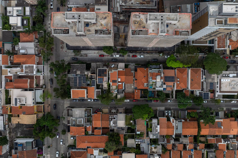 Fotografia feita de cima mostra o topo de prédios em construção e casas de telhados alaranjados em São Paulo. A imagem é ampla e compreende três fileiras de casas em ruas horizontais e uma fileira de casas na rua vertical, no lado esquerdo da imagem.