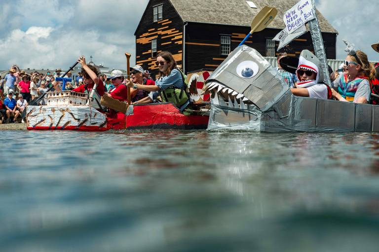 Imagem feita de dentro da água mostra pessoas se divertindo em barcos de papelão decorados.