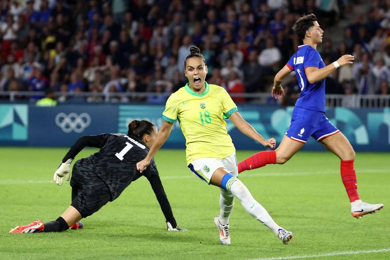 Gabi Portilho comemora gritando logo após marcar o seu gol nas quartas de final das Olimpíadas, contra a França. Ela está à frente da goleira francesa, caída no chão, e de uma outra jogadora, correndo ao fundo