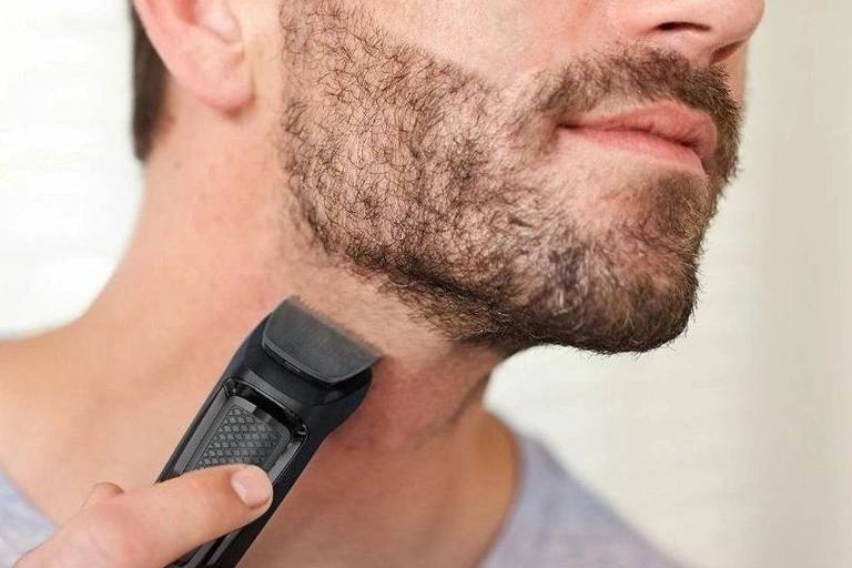 Imagem mostra em detalhe um homem fazendo a barba com um barbeador elétrico. A pele dele é clara e a barba marrom escuro.