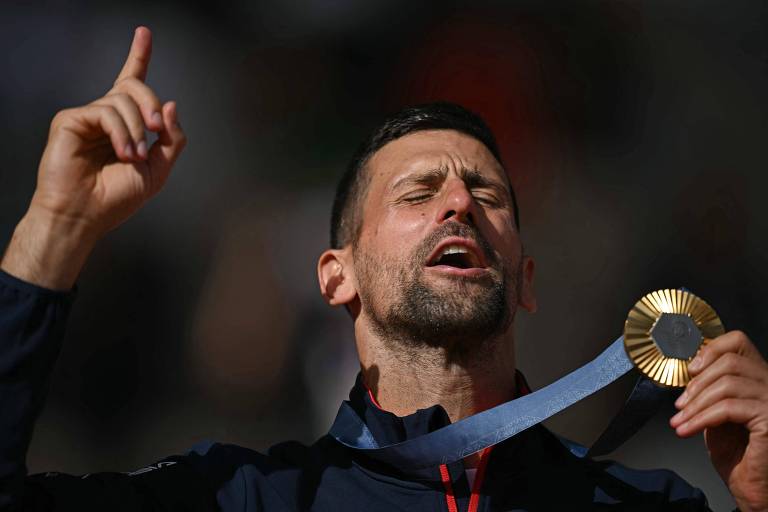 Tenista de olhos fechados segurando a medalha olímpica e com o dedo apontado para cima