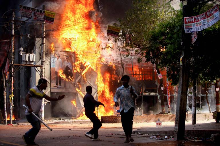 Imagem mostra manifestantes em confronto com a polícia enquanto um incêndio atinge um prédio