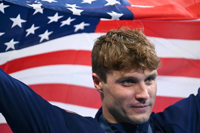 Bobby Finke, dos EUA, no pódio depois de ganhar os 1.500 m nado livre na Arena Paris La Défense, local das provas olímpicas; atrás dele está a bandeira norte-americana
