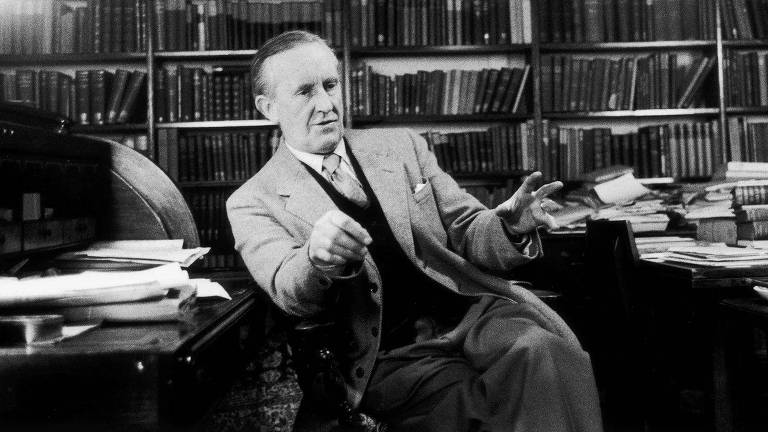 JRR Tolkien Tolkien sentado, conversando, com prateleiras de livros ao fundo