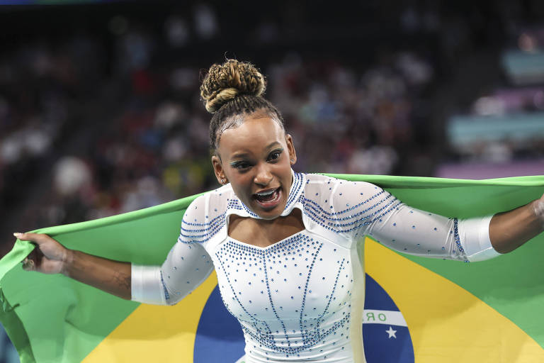 Na Arena Bercy, a ginasta Rebeca Andrade, com a bandeira do Brasil, comemora a prata no salto nas Olimpíadas de Paris