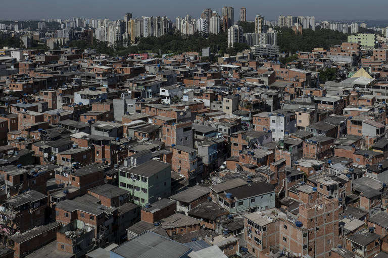 Imagem aérea mostra a favela de paraisópolis. A comunidade é composta por centenas de pequenas casa de alvenaria com tijolos à vista. Ao fundo, há alguns prédios. 